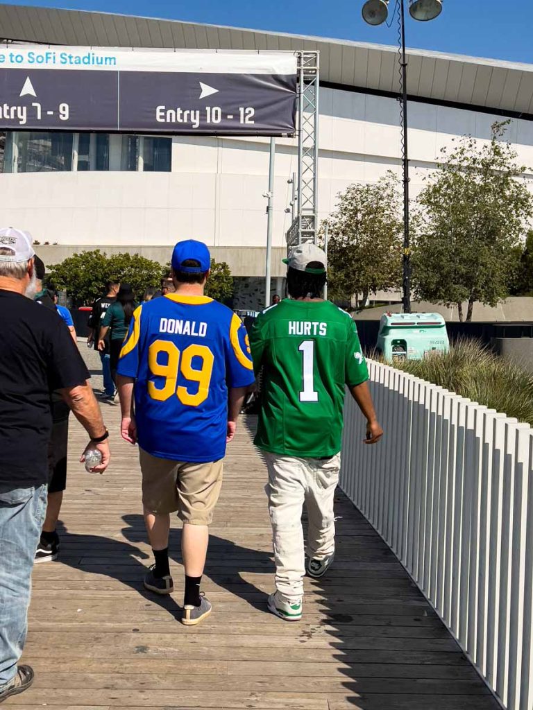 two friends enter SoFi Stadium - one wears a LA Rams jersey while the other wears a Philadelphia Eagles jersey.