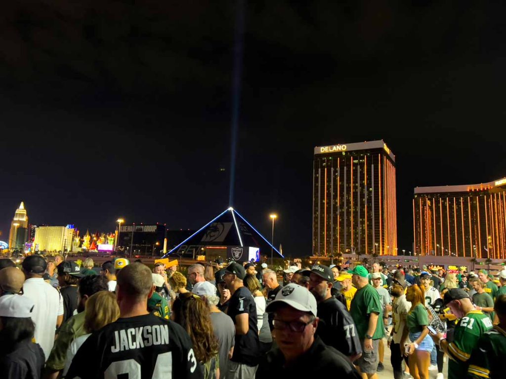 NFL fans leave Allegiant Stadium after a primetime football game. Mandalay Bay and the Luxor are lit up in the distance.
