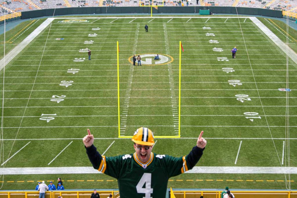 An excited Green Bay Packers fan in a Brett Favre jersey poses for a picture in the end zone of Lambeau Field.