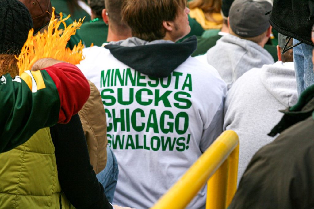 A green Bay Packers fan at Lambeau Field wears a white T-shirt with the caption, "Minnesota Sucks, Chicago Swallows".