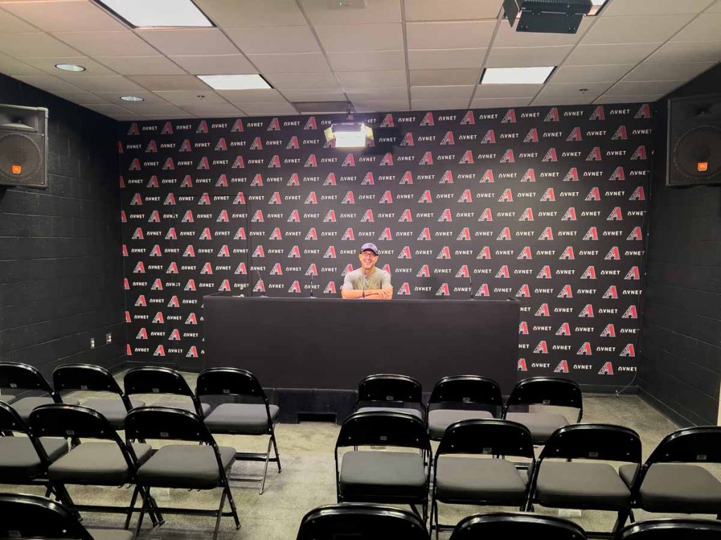 Dan Brewer, of the UltimateSportsRoadTrip travel blog, pretends to give an Arizona Diamondbacks press conference during a tour of Chase Stadium.